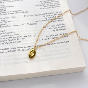 Detail of 18K gold-plated oval pendant with star engraving and zircon on vintage book page