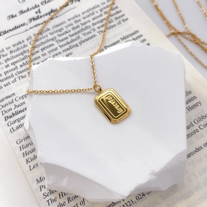 Detail of a 18K gold plated necklace with a rectangular tag and embossed graceful text