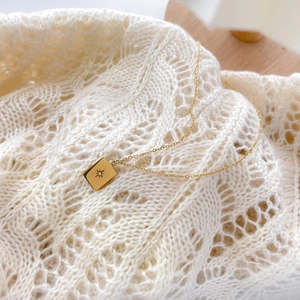 Close-up of 18K gold plated starburst pendant necklace on a white knit sweater