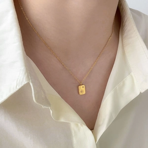 Close-up of a matte gold rectangular starburst pendant necklace worn on a model collar