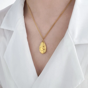 Vue détaillée d'un pendentif goutte à texture lave sur une chaîne dorée et chemise blanche