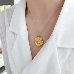 Détail d'un collier pendentif ailes d'ange plaqué or 18K porté avec une chemise blanche