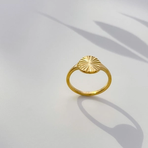 Vue détaillée d'une bague dorée avec disque à rayons solaires et textures radiales fines