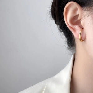 Vista macro di un earcuff minimalista in oro lucido indossato sulla cartilagine dell'orecchio