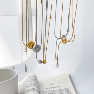 Détail de colliers minimalistes en acier titane avec pendentifs perles sur un livre ouvert