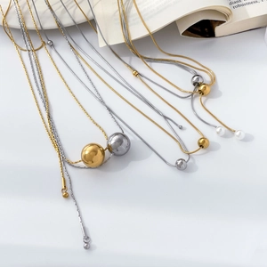 Collier minimaliste en acier titane avec sphères métalliques et perle sur un livre
