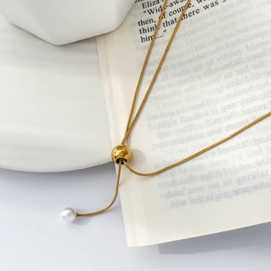 Détail du collier à chaîne serpent dorée avec fermoir boule réglable et perle blanche