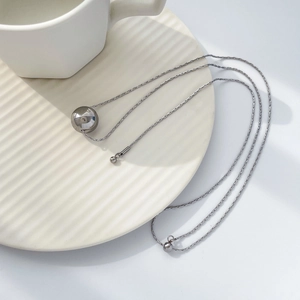 Détail d'un collier en acier titane argenté avec pendentif sphère creuse sur un plateau