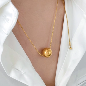 Gros plan d'un grand pendentif sphère dorée polie sur un collier en acier titane
