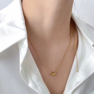 Collier minimaliste en chaîne serpent dorée avec pendentif boule polie sur un modèle