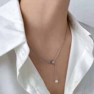 Détail d'un long collier argenté avec perle métallique et perle blanche sur chemise