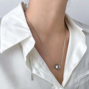 Collier à pendentif sphère argentée polie sur une chaîne sobre portée sur une chemise en soie
