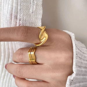 Detail von 18K vergoldeten, mehrlagigen, geschwungenen M-förmigen Ringen an einer Hand