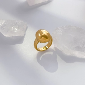 Close-up of golden minimalist domed pebble ring displayed on crystal stones in soft light