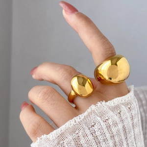 Polished gold pebble rings on finger with elegant lace sleeve in minimalist style