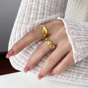 Gros plan d'une bague vague dorée et d'un anneau texturé sur main avec tricot blanc