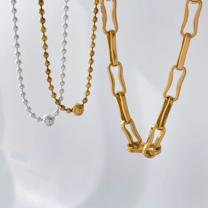 Detail of silver ball chains and gold paperclip necklace with polished metal texture