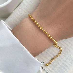 Detailed shot of a gold beaded bracelet with an adjustable chain on a model's wrist