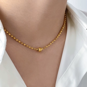 Close-up of minimalist gold beaded necklace with a central large bead on a silk shirt