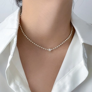 Macro detail of a silver beaded ball chain necklace featuring a large central polished bead