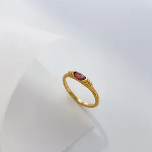 Detailed macro view of a gold ring featuring an oval red zircon and textured band