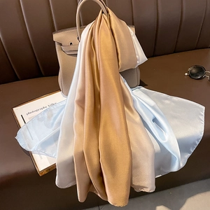 Detail of luxury gradient satin scarves draped over a leather bag on a sofa