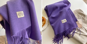 Detail of purple scarf with fringes and white woven tag next to an apricot blazer