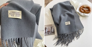 Detailed close-up of dark grey pashmina scarf texture and stitched brand label with fringes