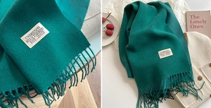 Detailed close-up of emerald green knitted scarf texture with fringes and fabric label