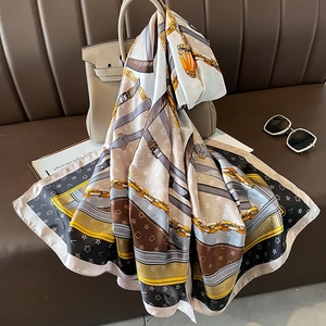 Elegant chain print silk scarf in beige and brown draped over a stylish handbag