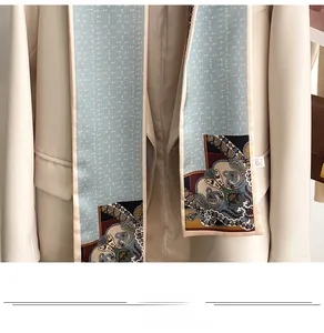 Close-up of a light blue silk scarf with paisley patterns styled on a beige blazer