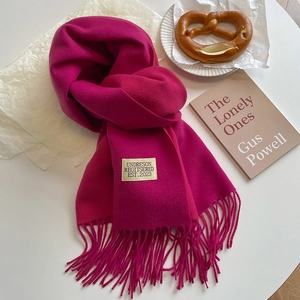 Detail of rose red cashmere feel scarf with long tassels and minimalist brand label