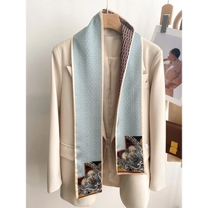 Detail of a light blue paisley printed narrow scarf styled on a beige blazer jacket