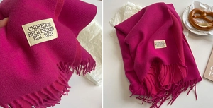 Detail of rose red cashmere feel scarf featuring long tassels and minimalist brand label