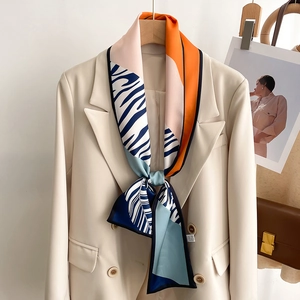 Silk scarf with zebra print and orange geometric patterns tied on a beige blazer collar