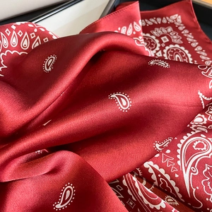 Detailed close-up showing the smooth satin texture and white paisley pattern on red silk scarf