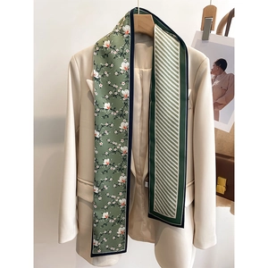 Détail d'un foulard en soie vert forêt avec imprimé magnolia blanc sur un blazer blanc