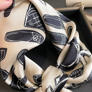 Detail view of beige silk scarf featuring elegant black camellia and shoe patterns
