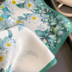 Elegant silk scarf with white camellia flower print and green rolled edges on dark background
