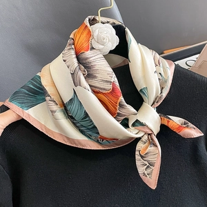 Elegant silk scarf with tropical leaf print tied on a black sweater neck as accessory