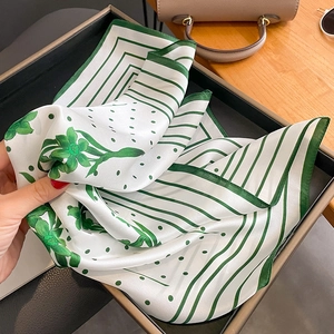 Foulard en soie aux motifs floraux verts présenté sur un plateau avec un sac à main
