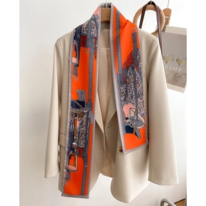 Détail d'un foulard twilly orange à motif équestre porté sur un blazer beige chic