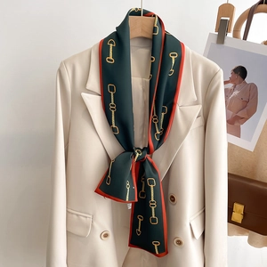 Foulard en soie vert foncé avec motif chaîne dorée et bord orange sur blazer blanc