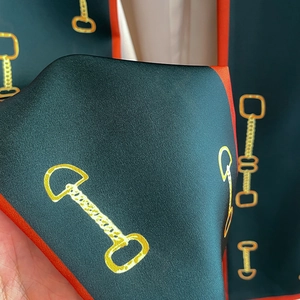 Vue macro d'un foulard en soie vert foncé avec motif mors et bords roulés orange