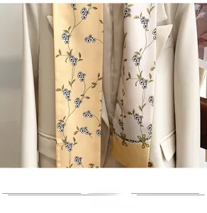 Détail d'un foulard étroit en soie fleurie abricot et crème avec un blazer beige
