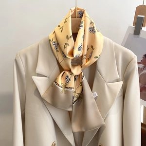 Détail d'un foulard en soie orange clair à fleurs noué sur un col de blazer beige