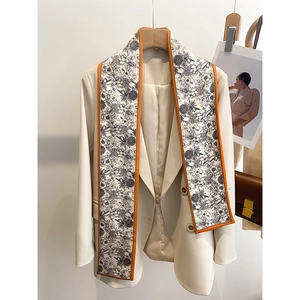 Gros plan d'un foulard twilly étroit à motif floral avec bordure orange sur blazer