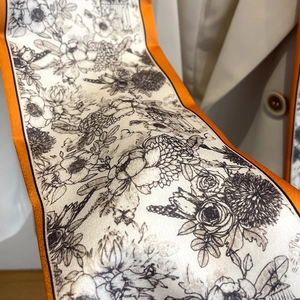 Détail d'un foulard étroit en soie à motif fleuri avec bordure orange contrastée