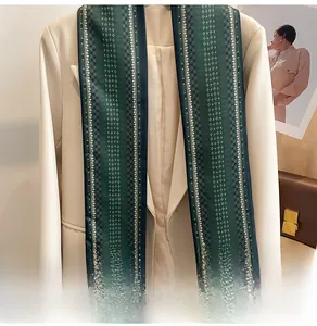 Détail d'un foulard étroit en soie verte à motifs dorés sur une veste blanche