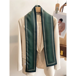 Détail d'une écharpe étroite vert foncé avec motifs géométriques sur un blazer